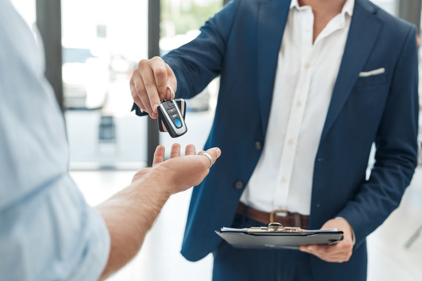 Young man buying new car taking keys from agent holding folder with documents close-up at salon